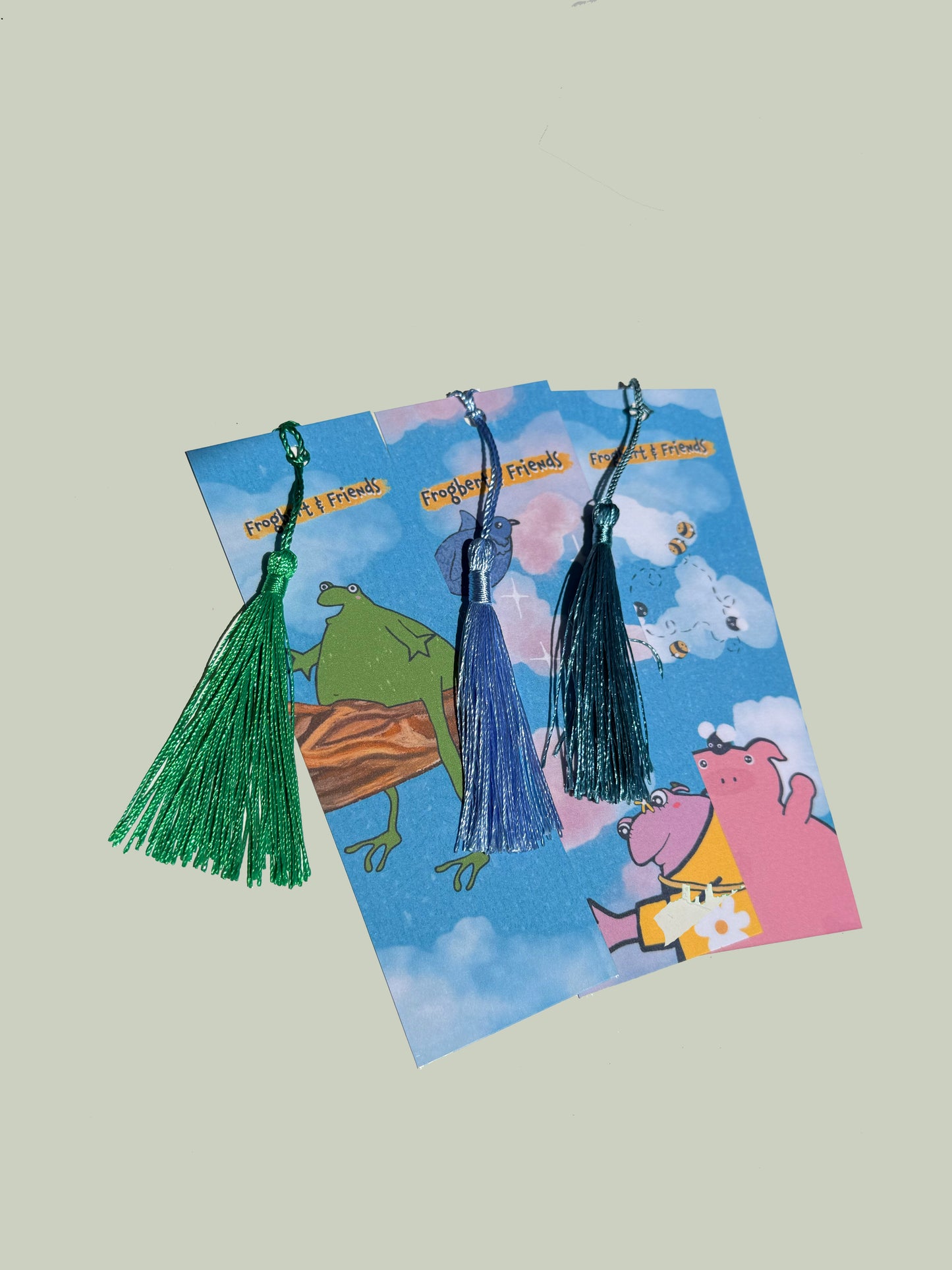 Three tassel bookmarks on a 'Frog and Friends' themed card with cartoon characters.